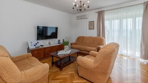 Una sala de estar con dos sillones color beige, una mesa de centro de madera, un televisor de pantalla plana, un aparador de madera y una araña.