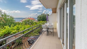 Un balcón con mesa y sillas, vista al mar y un jardín con parras.