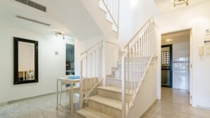 Ein geräumiger Korridor mit Marmorboden, einer weißen Treppe mit Geländer, einem Schreibtisch mit Stuhl und einem großen Spiegel an der Wand.