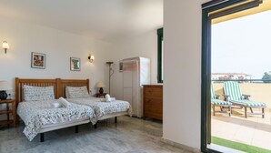 Ein Schlafzimmer mit Doppelbett, Nachttischen, einem Schminktisch und Blick auf den Balkon mit Liegestühlen.