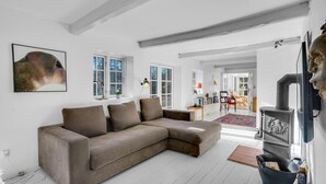 A modern living room with a sectional sofa, large windows, a fireplace, and a dining area in the background. - Cozy home in Højby with kitchen (Højby)