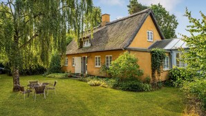 A traditional house with a thatched roof, surrounded by lush greenery and a well-maintained lawn. - Cozy home in Højby with kitchen (Højby)