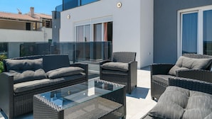 A modern outdoor patio with wicker furniture and a glass table, overlooking a residential area.