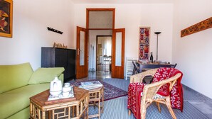 A living room with a green sofa, a wicker chair with a red cover, a wooden coffee table, and a dining area with a patterned rug. - Lovely apartment in Rimini with kitchen (Rimini)