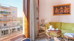 A balcony with a view of a building, a green sofa, a small table with a tray of tea items, and a painting on the wall. - Lovely apartment in Rimini with kitchen (Rimini)
