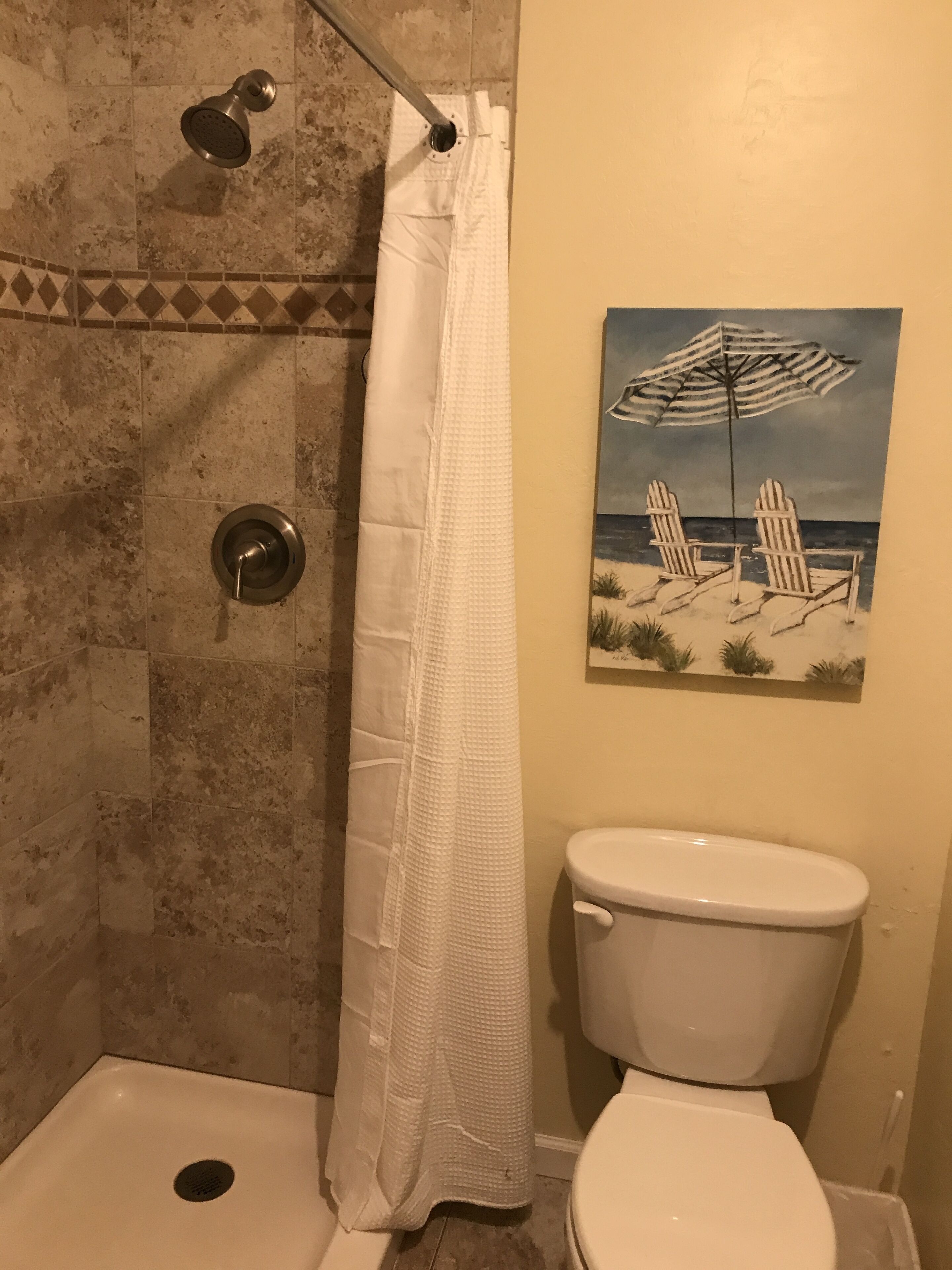 Un baño con ducha, inodoro y un cuadro con motivos marinos en la pared.