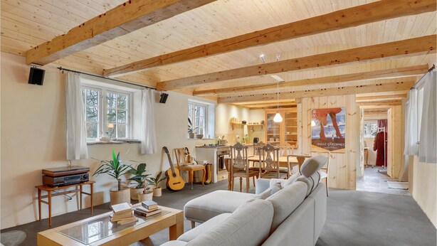Un salon chaleureux avec un canapé, une table basse et une guitare. On aperçoit, au fond, un coin cuisine avec une affiche accrochée au mur.