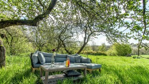 Un espace extérieur aménagé avec un canapé et une table, entouré d’une végétation luxuriante et d’arbres.