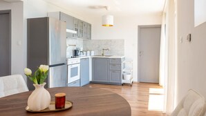 Una cocina moderna con armarios grises, un refrigerador de acero inoxidable, un lavamanos blanco y una lámpara colgante.