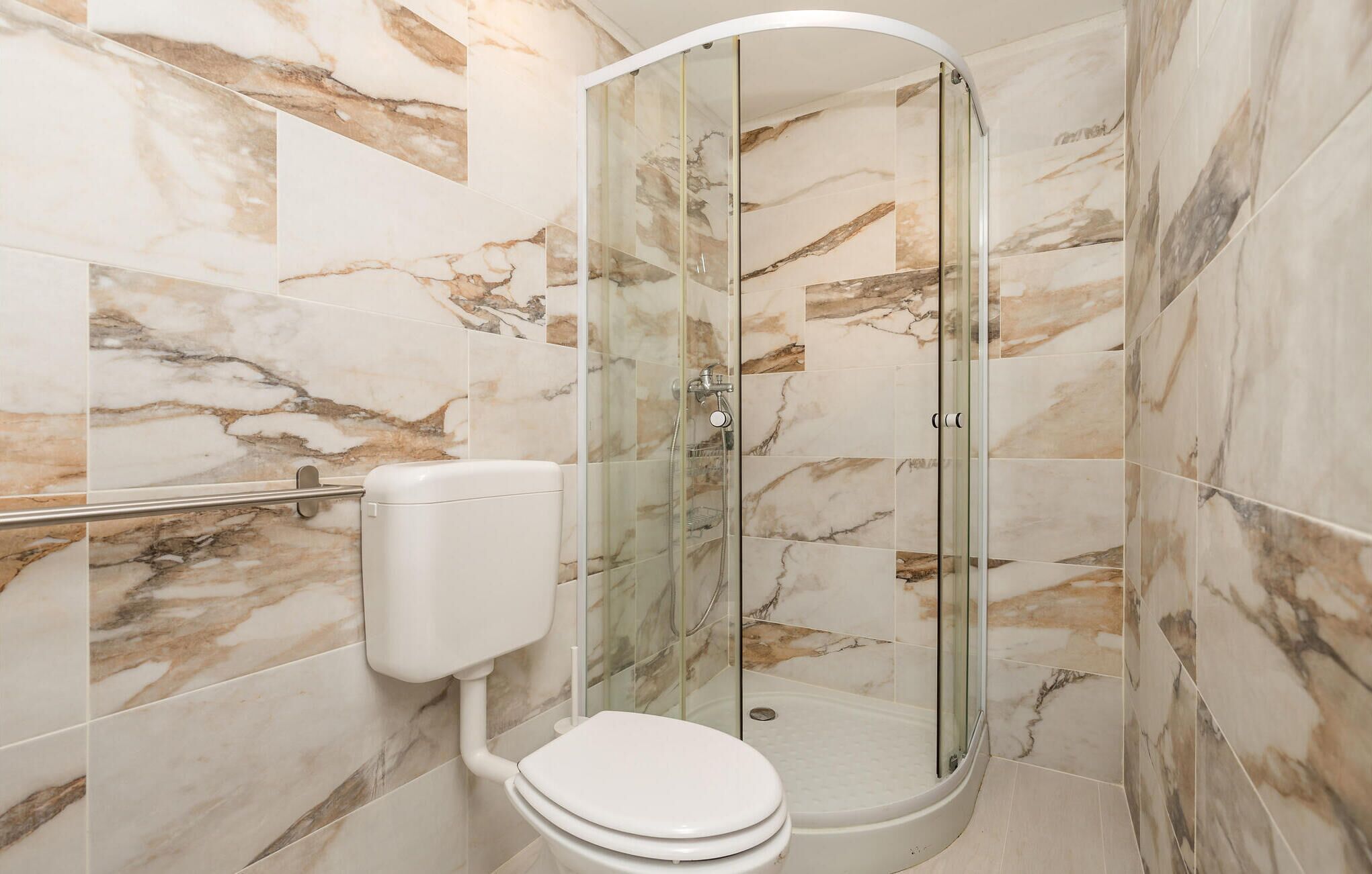 A modern bathroom with a glass-enclosed shower, marble tiles, and a toilet.