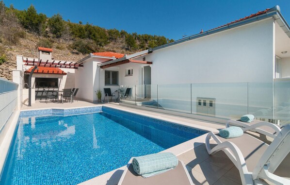 A swimming pool with a glass balustrade, lounge chairs, and a barbecue area. - Awesome home in Zrnovnica (Zrnovnica)