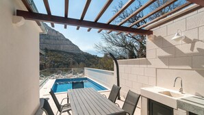 Zona junto a la piscina con mesa y sillas, un lavamanos integrado y una estructura de pérgola.
