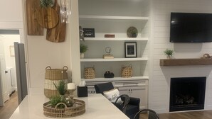 A modern kitchen with a large island, white cabinetry, and a built-in fireplace. - Beautiful new home at Kentucky Lake with community pool! Close to Murray State! (Murray)