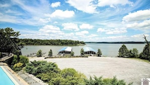 A lakeside view with a swimming pool, two covered structures, and a dock. - Beautiful new home at Kentucky Lake with community pool! Close to Murray State! (Murray)