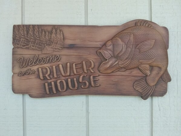 A wooden sign with a fish and trees, reading "Welcome to the RIVER HOUSE."