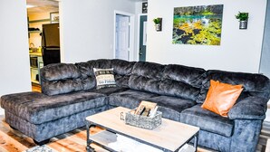Una sala de estar con un sofá seccional, una mesa de centro y una cocina al fondo.