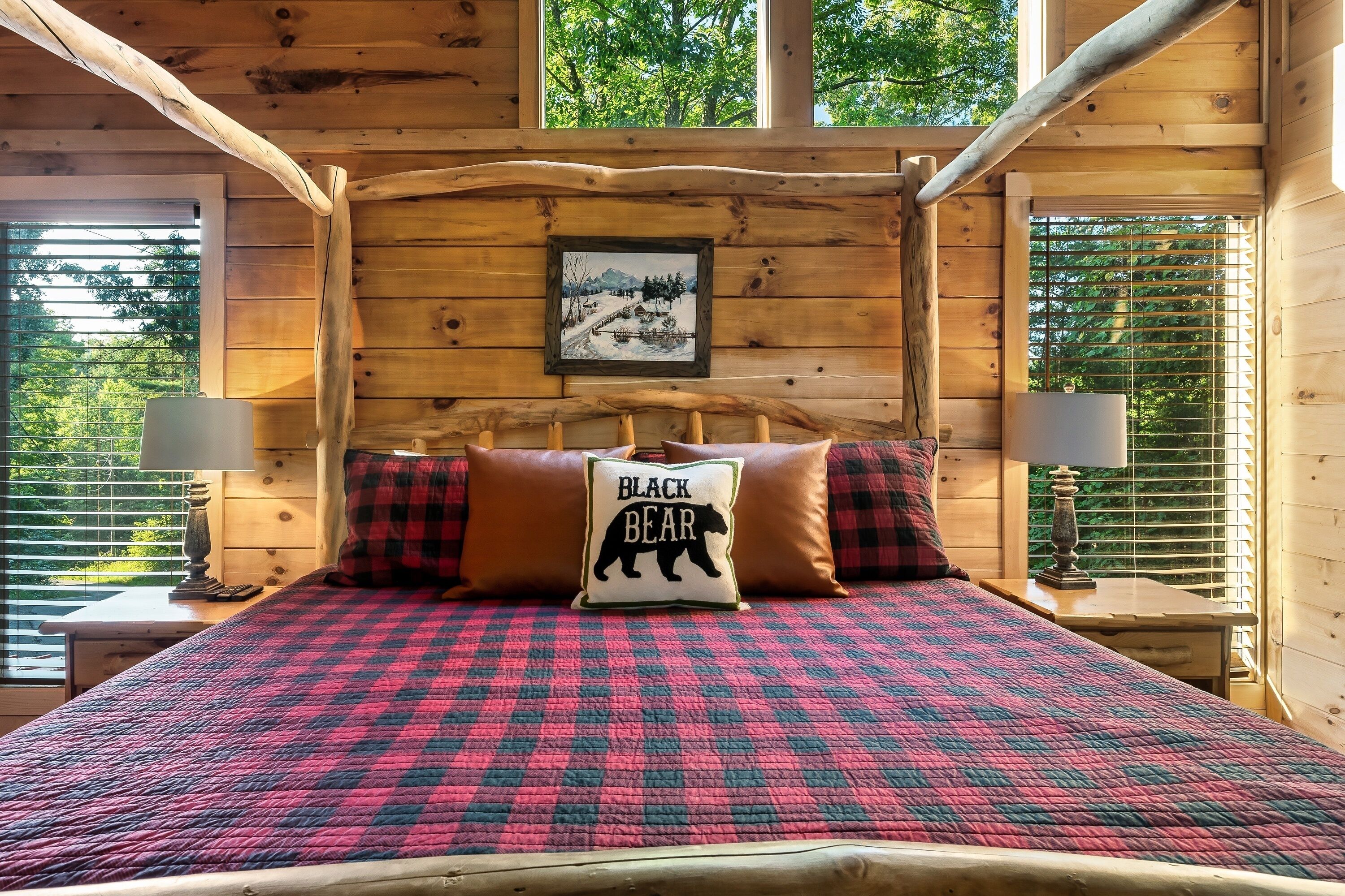Ein Schlafzimmer einer Holzhütte mit einem Bett, zwei Kissen, einem Nachttisch, einer Lampe und einem gerahmten Bild an der Wand.