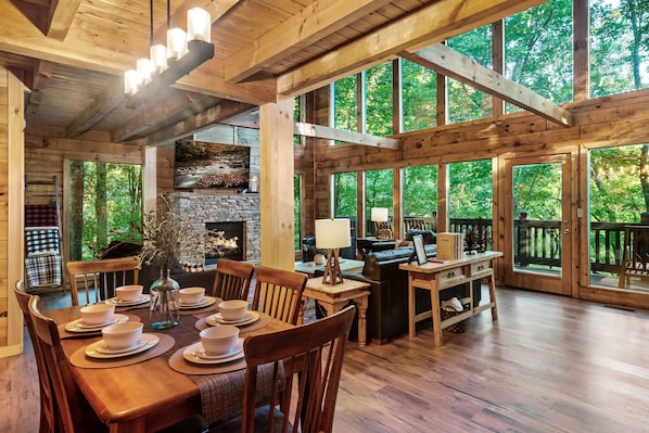 Un intérieur spacieux en bois, comprenant un coin repas, une cheminée et de grandes fenêtres donnant sur la forêt.