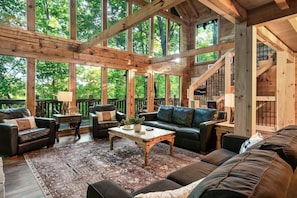 Un vaste espace de vie doté d’un grand plafond en bois, de nombreuses fenêtres offrant une vue sur l’extérieur et d’un coin salon confortable comprenant un canapé et des fauteuils.