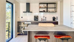 Une cuisine moderne dotée d’un grand îlot central, de tabourets de bar et offrant une vue à travers une porte vitrée.