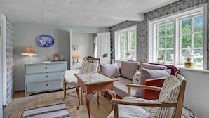 A cozy living room with a wooden sofa, a small table, and a chair. There is a window with a view of greenery outside.