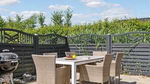 Eine Terrass mit Tisch, Stühlen, einem Grill und einem Tor.