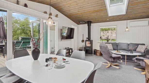 A modern living room with a fireplace, a dining area, and a TV mounted on the wall. - Amazing home in Brovst with kitchen (Brovst)