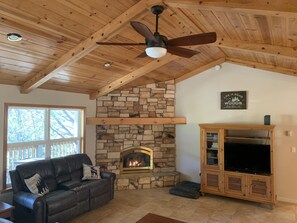 Un salon chaleureux avec une cheminée en pierre, un canapé en cuir, un meuble de rangement en bois et un ventilateur de plafond.