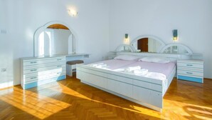A bedroom with a bed, two dressers, a vanity with mirrors, and a wooden ceiling.