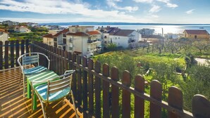 A terrace with a view of a coastal town, featuring a wooden fence and a chair.