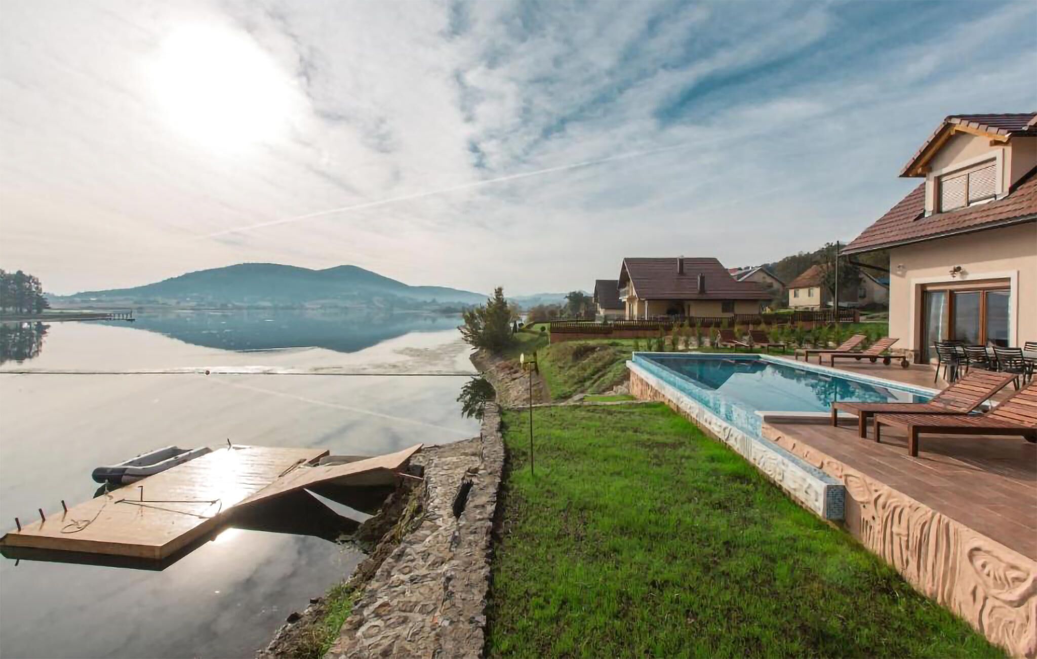 A lakeside property with a swimming pool, a dock, and houses with a view of the lake and mountains.