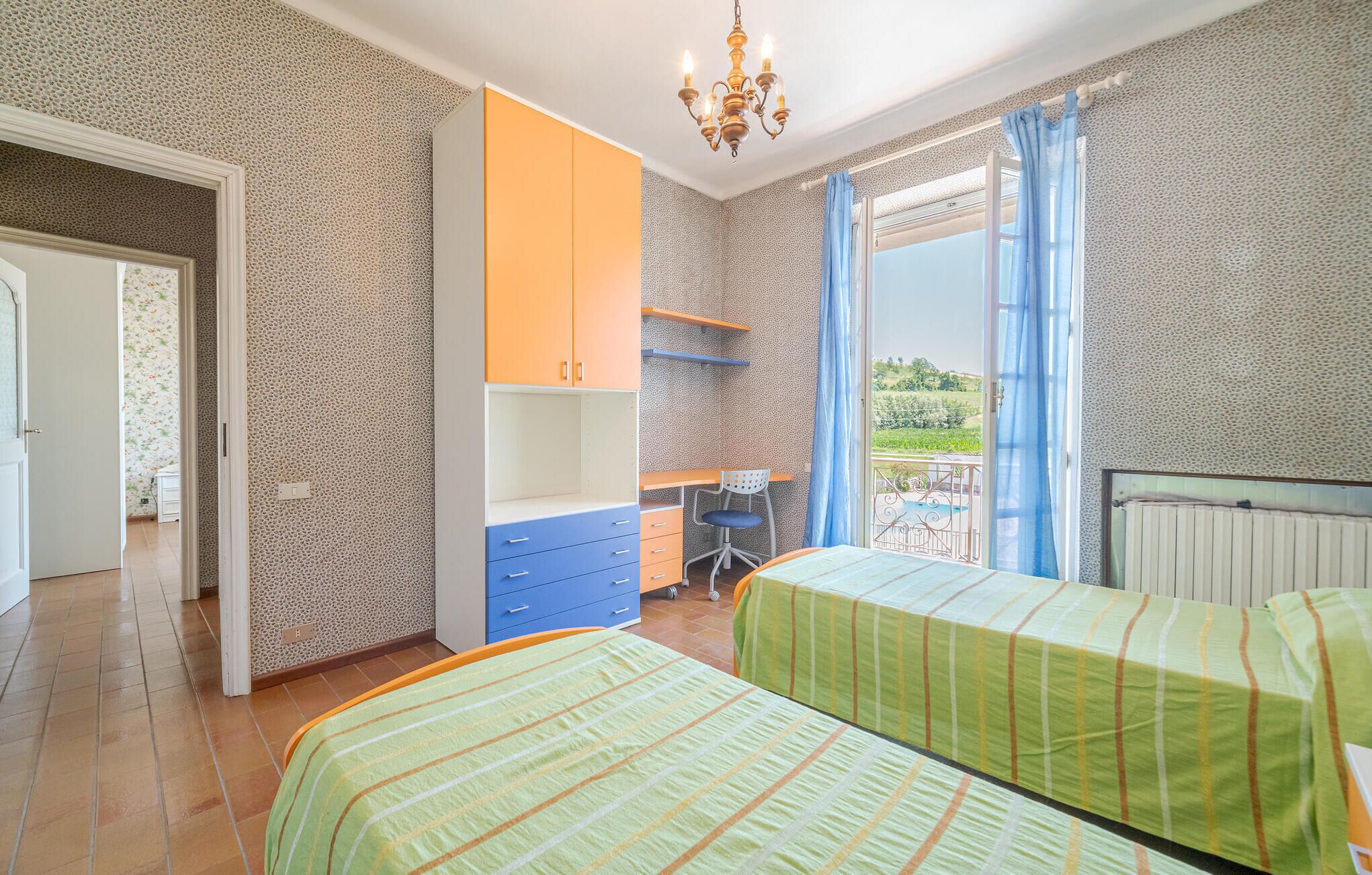 Un dormitorio con dos camas, un escritorio y una silla. Hay una ventana con cortinas y vistas a la vegetación exterior.