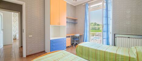 Un dormitorio con dos camas, un escritorio y una silla. Hay una ventana con cortinas y vistas a la vegetación exterior.