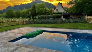 Una piscina con un flotador con forma de cocodrilo, rodeada por un suelo de piedra y una valla de madera.