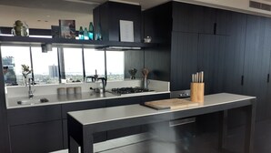 A modern kitchen with a large island, stainless steel appliances, and a view of the city through large windows. - Top Floor Stunning Views (South Melbourne)