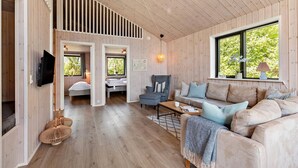 A cozy cabin interior with a wooden interior, a sofa, a chair, a coffee table, and a TV mounted on the wall. - Amazing home in Sydals with sauna (Sydals)