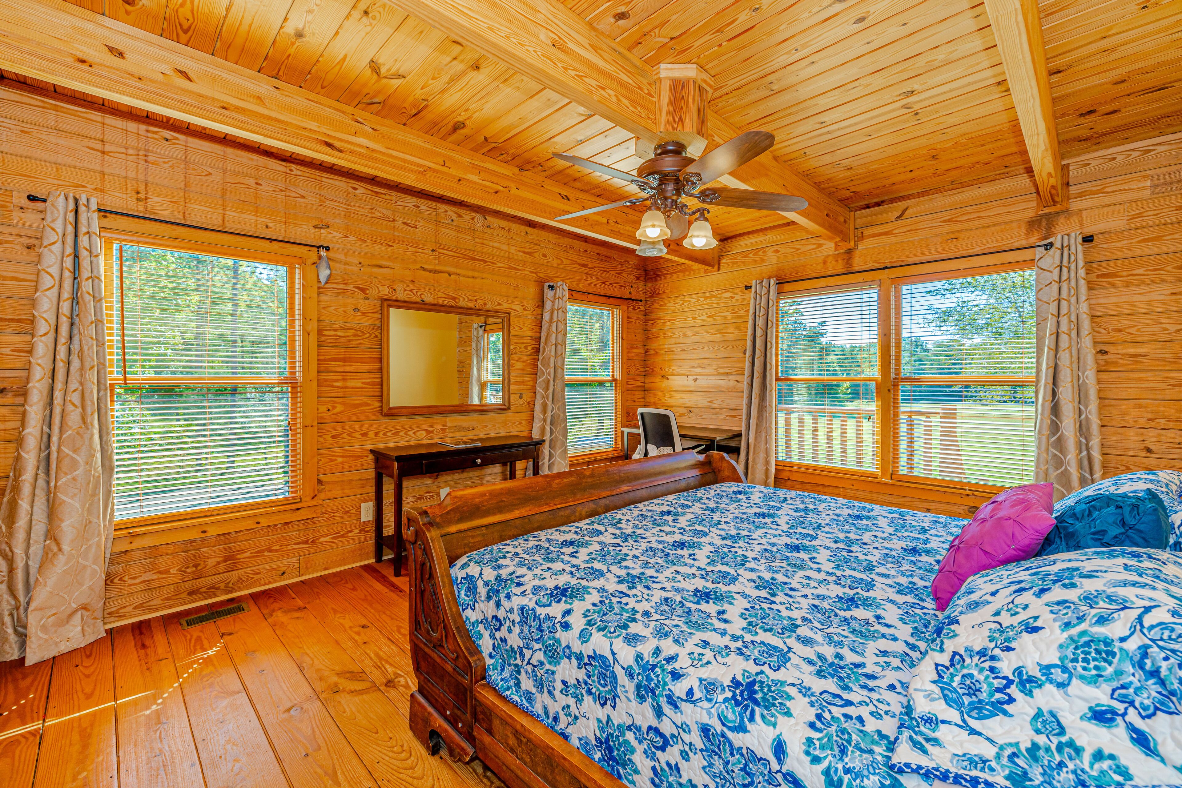 A wooden cabin bedroom with a bed, a desk, and a ceiling fan.
