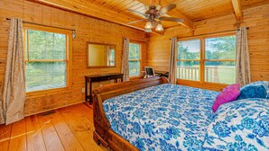 A wooden cabin bedroom with a bed, a desk, and a ceiling fan.