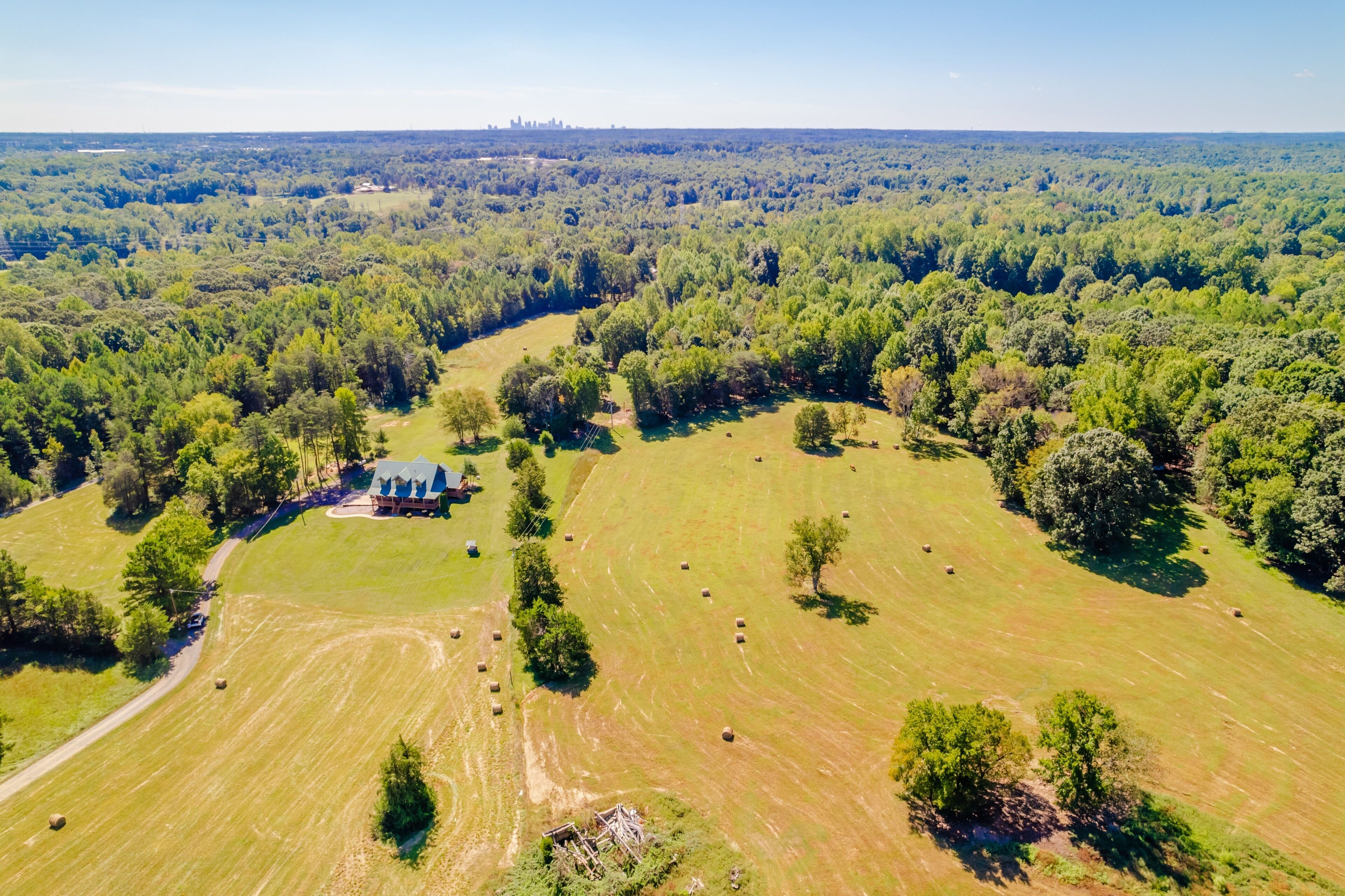 An aerial view of a rural property with a large open field, scattered trees, and a small building with a blue roof.
