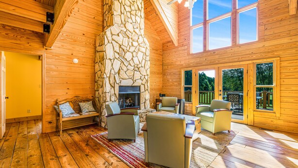 A log cabin interior with a stone fireplace, wooden floors, and a deck area.