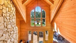 A wooden interior with a stone wall, a ceiling fan, and large windows.