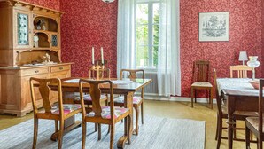 Une salle à manger avec une table et des chaises en bois, un radiateur et une fenêtre avec des rideaux.
