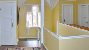 Un couloir aux murs jaunes, aux portes blanches et à la fenêtre ornée d’un rideau.