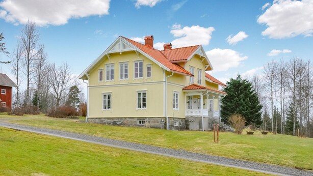Une maison à deux étages, avec un toit recouvert de tuiles rouges, un porche et des fondations en pierre.