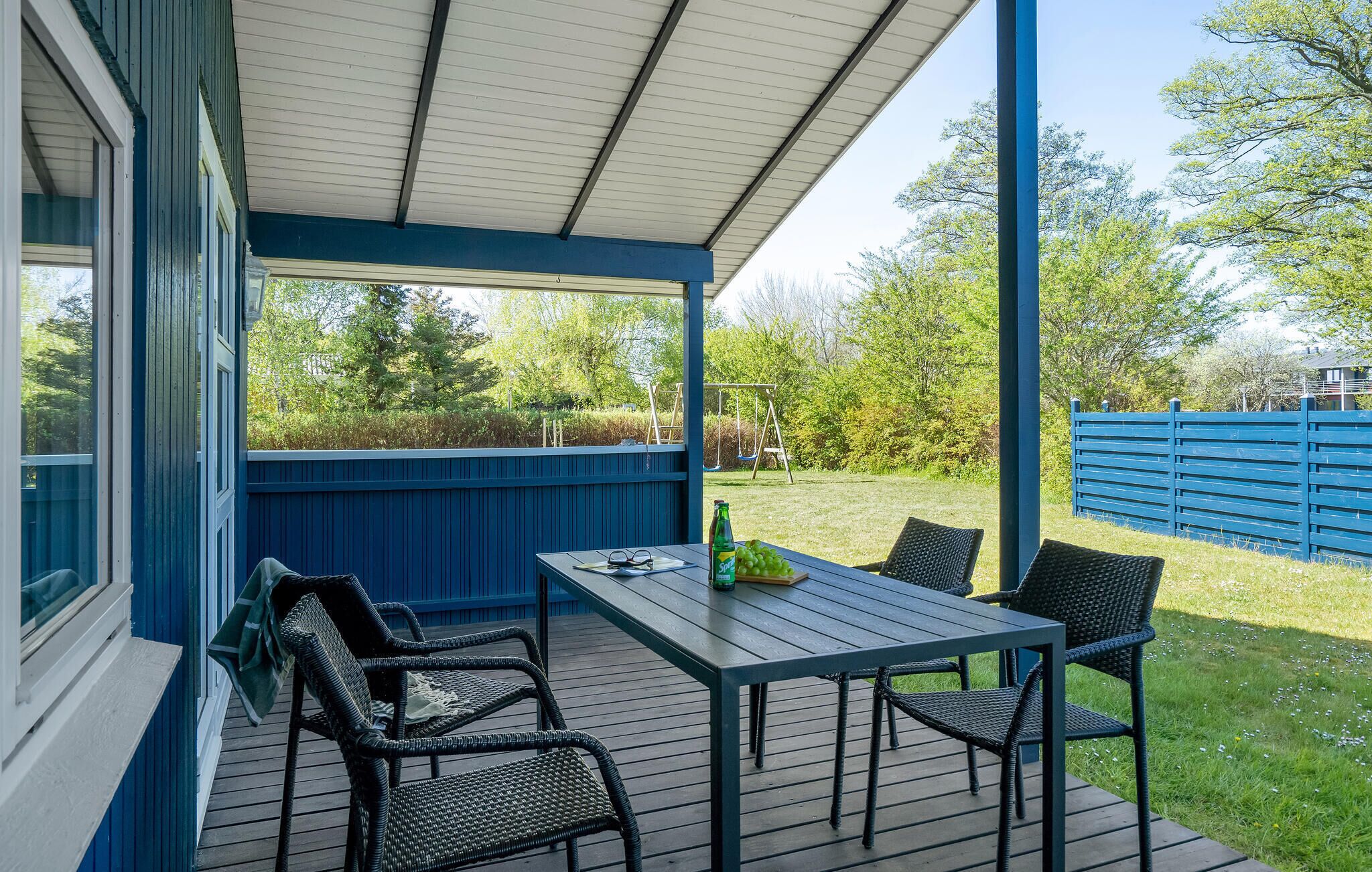 Eine überdachte Terrasse mit Tisch und Stühlen, einer Schaukel und einem blauen Zaun im Hintergrund.