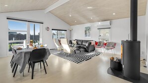 A modern living room with a dining area, large windows, a fireplace, and a loft-style ceiling. - Nice home in Skælskør with sauna (Skælskør)