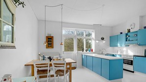 Une cuisine moderne avec des meubles bleus, un plan de travail blanc et un coin repas comprenant une table et des chaises en bois.