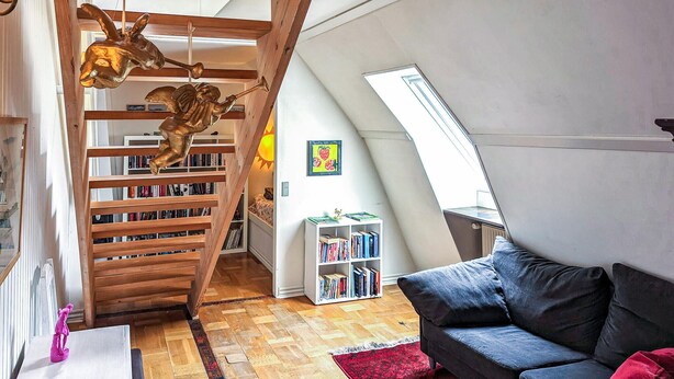 Un espace de vie de style loft avec un escalier en bois, des étagères, un canapé et une lucarne.