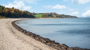 Une plage côtière avec une rive sinueuse, une digue rocheuse et une colline lointaine parsemée de bâtiments.