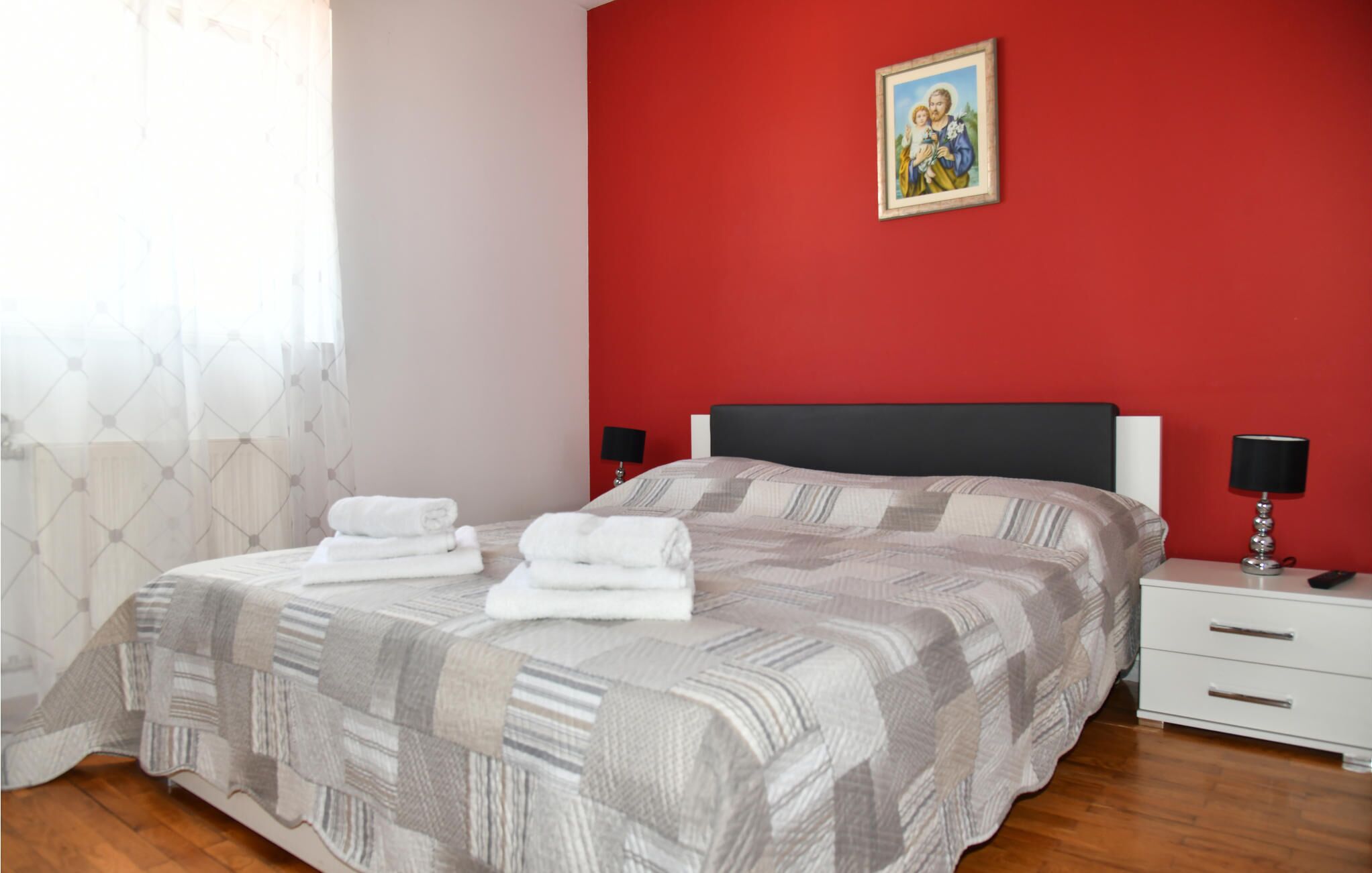 Quarto com parede vermelha, cama com manta listrada, duas mesas de cabeceira com abajures e um quadro emoldurado acima da cama.